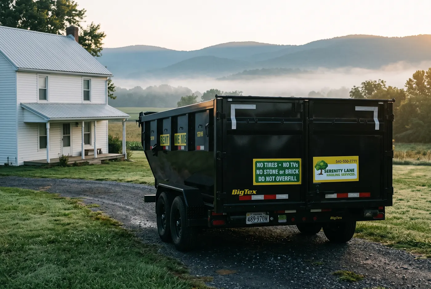 Serenity Lane Hauling's black dump trailer parked in a farmhouse driveway with misty Shenandoah ridgelines behind